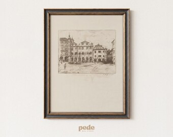 May include: A framed black and gold print of a European town square. The artwork is a detailed etching in shades of brown and beige, depicting buildings and figures. The frame is rectangular with a dark border.