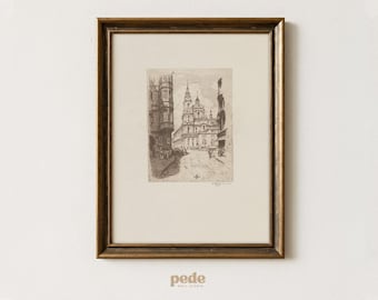 May include: A framed black and white etching of a European city scene. The artwork depicts buildings and a street with figures, set within a gold-toned wooden frame. The print is on a cream-colored background.