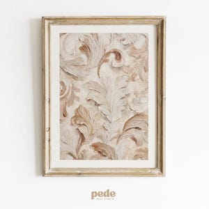 Puede incluir: Obra de arte enmarcada con un patrón texturizado detallado de hojas y volutas estilizadas en tonos beige y marrón. La obra de arte está enmarcada en un marco dorado, creando una estética clásica. La obra de arte es de pede wall studio.