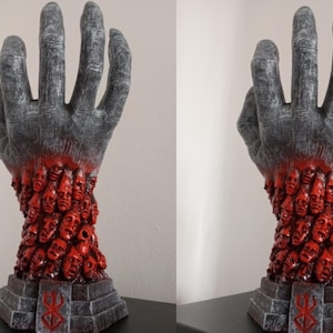 May include: A gray hand sculpture with a red base. The hand is holding a large number of small, red faces. The base has a black and white symbol on it.