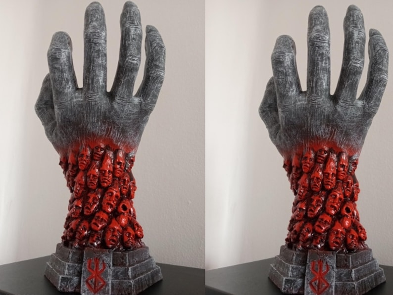May include: A gray hand sculpture with a red base. The hand is holding a large number of small, red faces. The base has a black and white symbol on it.