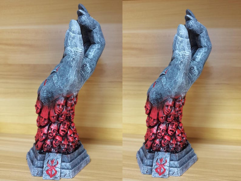 May include: A gray hand sculpture with a textured surface. The hand is holding a collection of small, red faces. The sculpture is on a gray base with a red symbol.