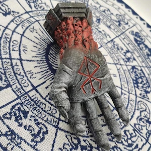 May include: A gray hand sculpture with a red symbol on the palm. The hand is covered in small, red, skull-like figures.