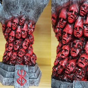 May include: A black hand sculpture with a base featuring the Berserk manga logo. The hand is covered in a swirling mass of red faces.