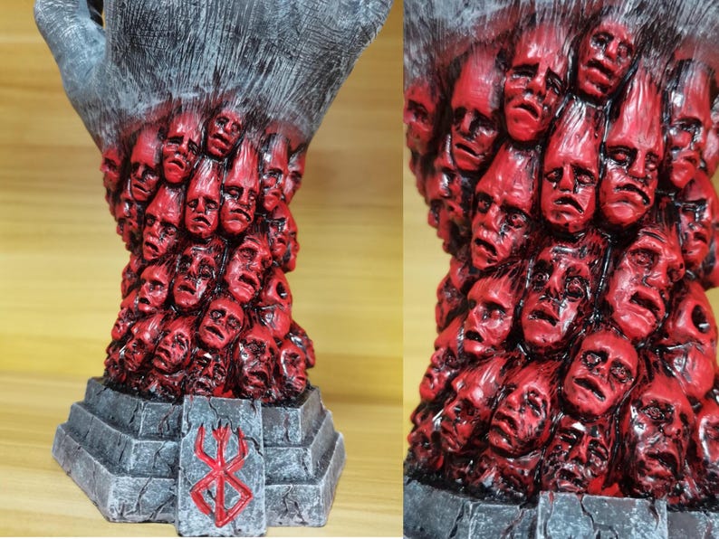 May include: A black hand sculpture with a base featuring the Berserk manga logo. The hand is covered in a swirling mass of red faces.