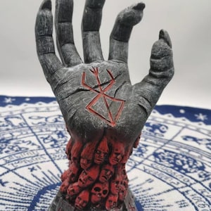 May include: A gray hand sculpture with a red symbol on the palm. The hand is holding a base made of many small faces.