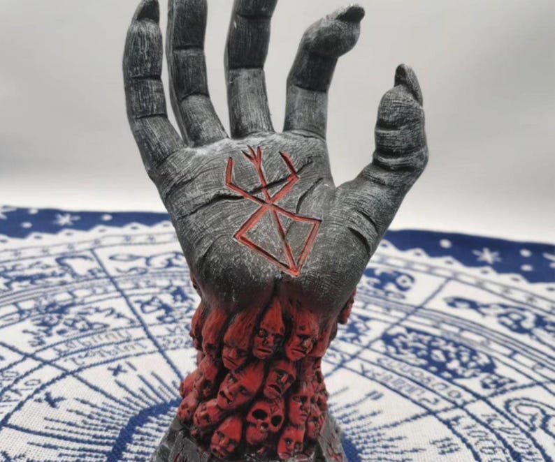 May include: A gray hand sculpture with a red symbol on the palm. The hand is holding a base made of many small faces.