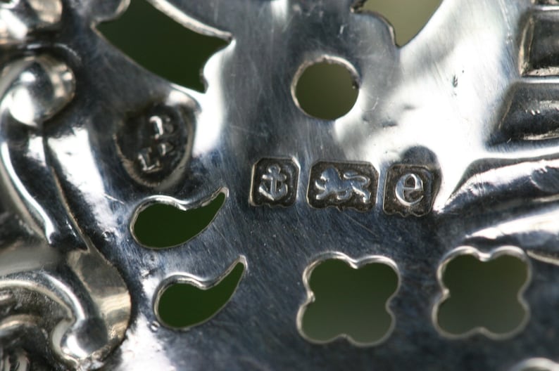 Puede incluir: Primer plano de los contrastes de plata en una pieza de joyer&iacute;a. Los contrastes incluyen un le&oacute;n, un ancla y la letra "e".