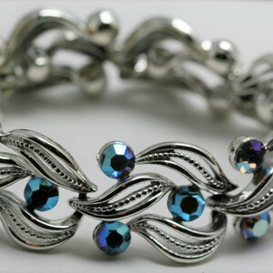 May include: A silver bracelet with a leaf design and blue iridescent stones.