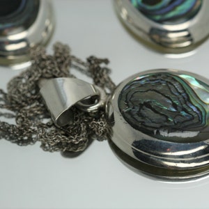 May include: A silver chain necklace with a pendant featuring a round abalone shell with iridescent green, blue, and black colors.