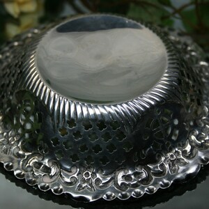 Puede incluir: Un cuenco de plata con un intrincado dise&ntilde;o calado alrededor del borde. El cuenco tiene una superficie lisa y reflectante y una base decorativa y estampada.