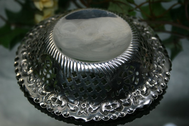 Puede incluir: Un cuenco de plata con un intrincado dise&ntilde;o calado alrededor del borde. El cuenco tiene una superficie lisa y reflectante y una base decorativa y estampada.
