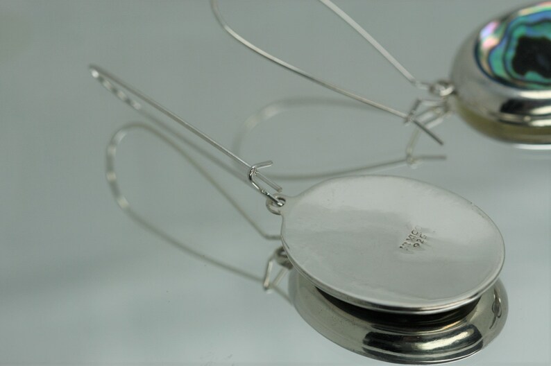 May include: A pair of silver earrings with a round, iridescent abalone shell inlay. The earrings have a simple, elegant design and are perfect for everyday wear.