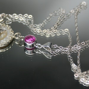May include: A silver chain necklace with two pendants. One pendant is a round, pink gemstone. The other pendant is a white shell with a silver star in the center.