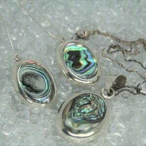 May include: A set of three silver oval pendants with iridescent abalone shell inlays. The pendants are on a silver chain and a pair of silver earring hooks.