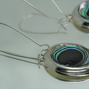 May include: A pair of silver earrings with a round abalone shell design. The earrings have a silver hook closure.