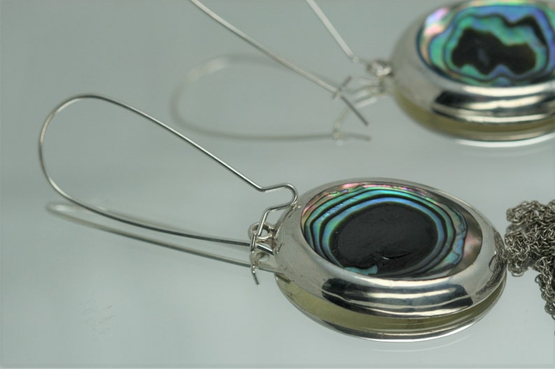 May include: A pair of silver earrings with a round abalone shell design. The earrings have a silver hook closure.
