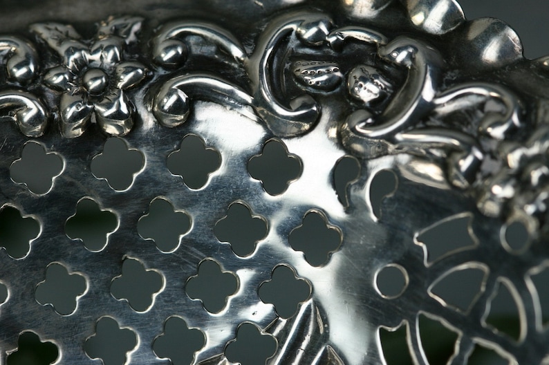 Puede incluir: Primer plano de un colador de plata con un dise&ntilde;o floral y una superficie perforada. El colador tiene un acabado met&aacute;lico brillante.