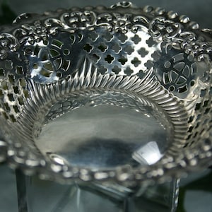 Puede incluir: Un cuenco de plata calado con un borde decorativo festoneado. El cuenco est&aacute; hecho de un delicado dise&ntilde;o de filigrana con una superficie lisa y reflectante.