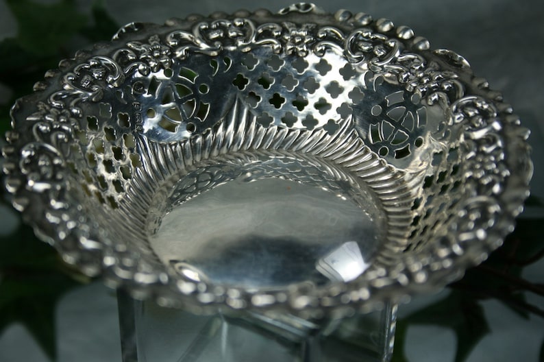 Puede incluir: Un cuenco de plata calado con un borde decorativo festoneado. El cuenco est&aacute; hecho de un delicado dise&ntilde;o de filigrana con una superficie lisa y reflectante.