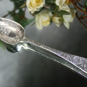 May include: A silver spoon with an ornate, swirling design. The spoon has a rounded bowl and a long, slender handle.