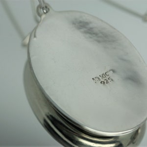 May include: The back of a silver oval pendant with the inscription "MEXIC 925".