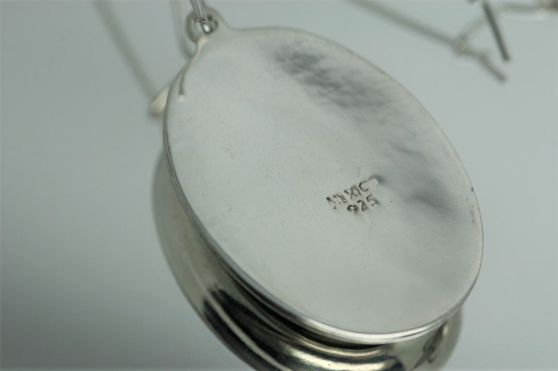 May include: The back of a silver oval pendant with the inscription "MEXIC 925".