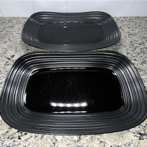 Puede incluir: Dos fuentes rectangulares. La fuente superior es de color gris oscuro y la inferior es negra. Ambas tienen un borde acanalado y elevado. Las fuentes están sobre una encimera moteada.