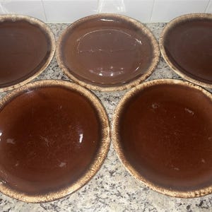 May include: Five brown ceramic plates with a glossy finish and a lighter brown, textured rim. The plates are arranged on a speckled countertop. These plates are suitable for serving food.