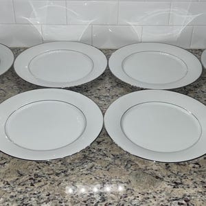 Puede incluir: Juego de ocho platos llanos blancos con un fino borde plateado.