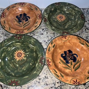 May include: Four decorative ceramic bowls with floral designs. The bowls feature a mix of colours, including brown, green, and orange, with a central flower motif in blue or yellow. The rims are decorated with red and green accents.