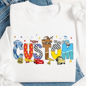 May include: White sweatshirt with a colorful graphic of the word "CUSTOM" made up of cartoon cars and trucks. The letters are in different colors and have various car-themed details.