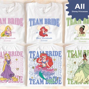 Può includere: T-shirt bianche con la scritta "Team Bride" in rosa, blu e verde, con grafiche di principesse Disney. Ogni maglietta include la scritta "Est. 2025" e "Ava's Bachelorette, Stafford". Le magliette mostrano Rapunzel, Ariel e Tiana.