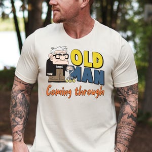 Könnte beinhalten: Ein weißes T-Shirt mit einem Cartoon-Bild eines älteren Mannes mit einem Rollator. Der Text "OLD MAN coming through" ist auf dem Shirt aufgedruckt.