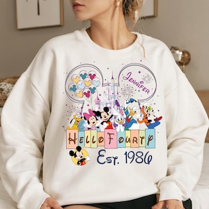 May include: A white sweatshirt featuring a colorful graphic of Disney characters, including Mickey and Minnie Mouse, Donald Duck, and Goofy. The design includes the text "Hello Fourth" and "Est. 1986", with the name "Jennifer" above the characters.