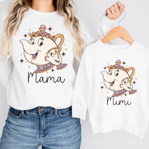 Peut inclure: Chemise à manches longues blanches avec une image de dessin animé d'une théière avec un visage. Le t-shirt de gauche dit "Mama" et le t-shirt de droite dit "Mimi".