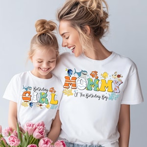 Può includere: Due magliette bianche con testo colorato e grafiche di creature marine. Una maglietta dice "Birthday GIRL" e l'altra "MOMMY Of The Birthday Boy". Le magliette sono indossate da una madre e una figlia.