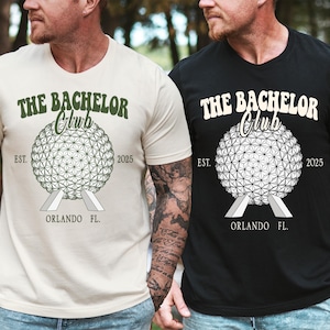 Op de afbeelding: Twee T-shirts, één beige en één zwart, elk met de tekst "THE BACHELOR Club" boven een geometrisch bolontwerp. Daaronder de woorden "EST. 2025 ORLANDO FL."