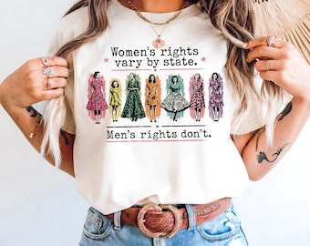 Puede incluir: Una camiseta color crema con un gráfico de siete figuras con vestidos de estilo vintage. El texto dice: Women's rights vary by state. Men's rights don't. El diseño incluye detalles de pinceladas en rosa y verde azulado detrás de las figuras.
