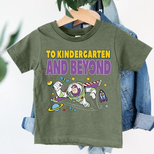 A green t-shirt with a cartoon character and text printed on it, hanging on a clothing hanger.