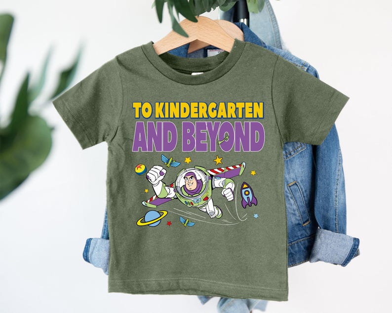 A green t-shirt with a cartoon character and text printed on it, hanging on a clothing hanger.