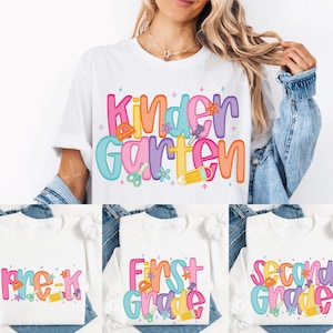 May include: White t-shirts with colorful text and school-themed graphics. One shirt says "Kindergarten", while others say "Pre-K", "First Grade", and "Second Grade". The designs include pencils, scissors, and flowers.