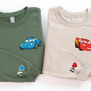 two sweatshirts with cartoon car designs, one green and one beige.