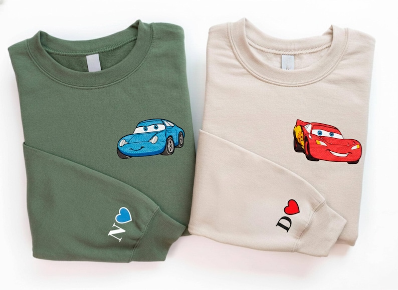 two sweatshirts with cartoon car designs, one green and one beige.