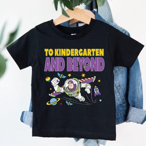 A black t-shirt with a colorful graphic of a character from the Toy Story franchise, along with the text "TO KINDERGARTEN AND BEYOND" printed on it.