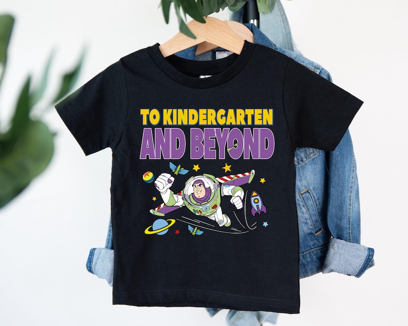 A black t-shirt with a colorful graphic of a character from the Toy Story franchise, along with the text "TO KINDERGARTEN AND BEYOND" printed on it.
