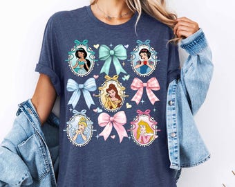 Peut inclure: Un t-shirt bleu marine avec un motif de princesses Disney dans des cadres avec des nœuds. Les princesses incluent Cendrillon, Blanche-Neige, Belle, Jasmine et Ariel.