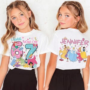 May include: White t-shirts with a colorful princess design. The front of the shirt has the text "I WAS 67 NOW I'M" with princess graphics. The back of the shirt says "JENNIFER" with princess graphics.