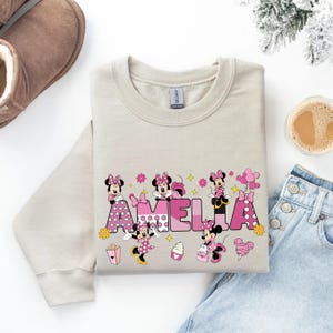 A gray sweatshirt with a personalized name printed on it, along with a pair of jeans and a pair of boots, as well as a cup of coffee and a snowflake decoration.