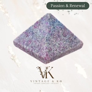 May include: A pyramid-shaped crystal with a textured surface, displaying a mix of purple, pink, and blue tones. The top of the image has the text "Passion & Renewal". The bottom of the image has the text "VINTAGE & KO" and "VINTAGE | JEWELLERY | CRYSTALS".